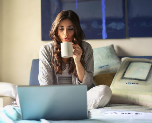 woman-in-bed-drinking-coffee-looking-at-homes-online