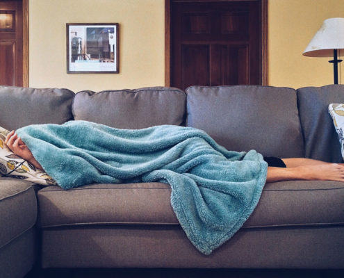 college-student-with-blanket-over-their-head-asleep-on-the-couch