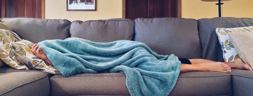 college-student-with-blanket-over-their-head-asleep-on-the-couch