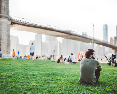 man sitting in park looking over Brooklyn Bridge